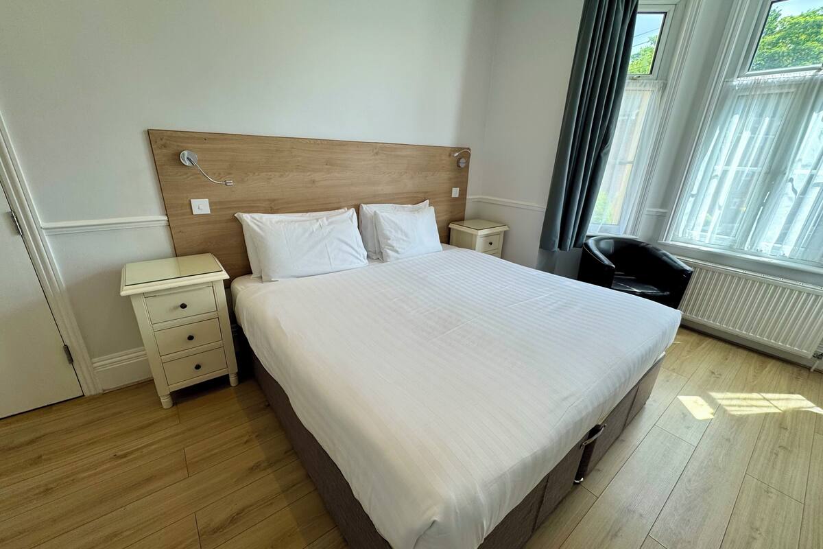 Un lit bien fait, avec une tête de lit en bois, une table de chevet dotée de tiroirs et une chaise.