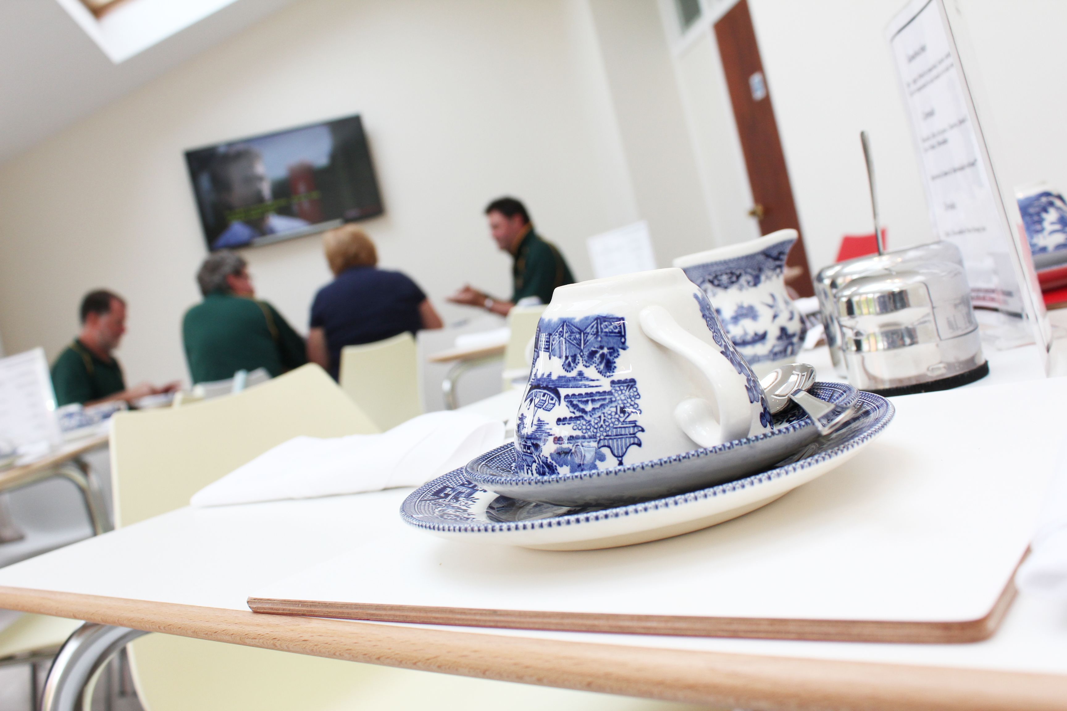 Una mesa de comedor con una taza y platillo de cerámica azul y blanco, un vaso de agua y un atril para el menú.