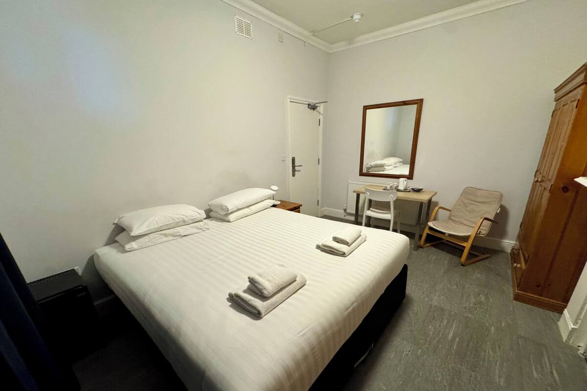Une chambre d’hôtel avec un lit, un bureau, une chaise et une armoire.