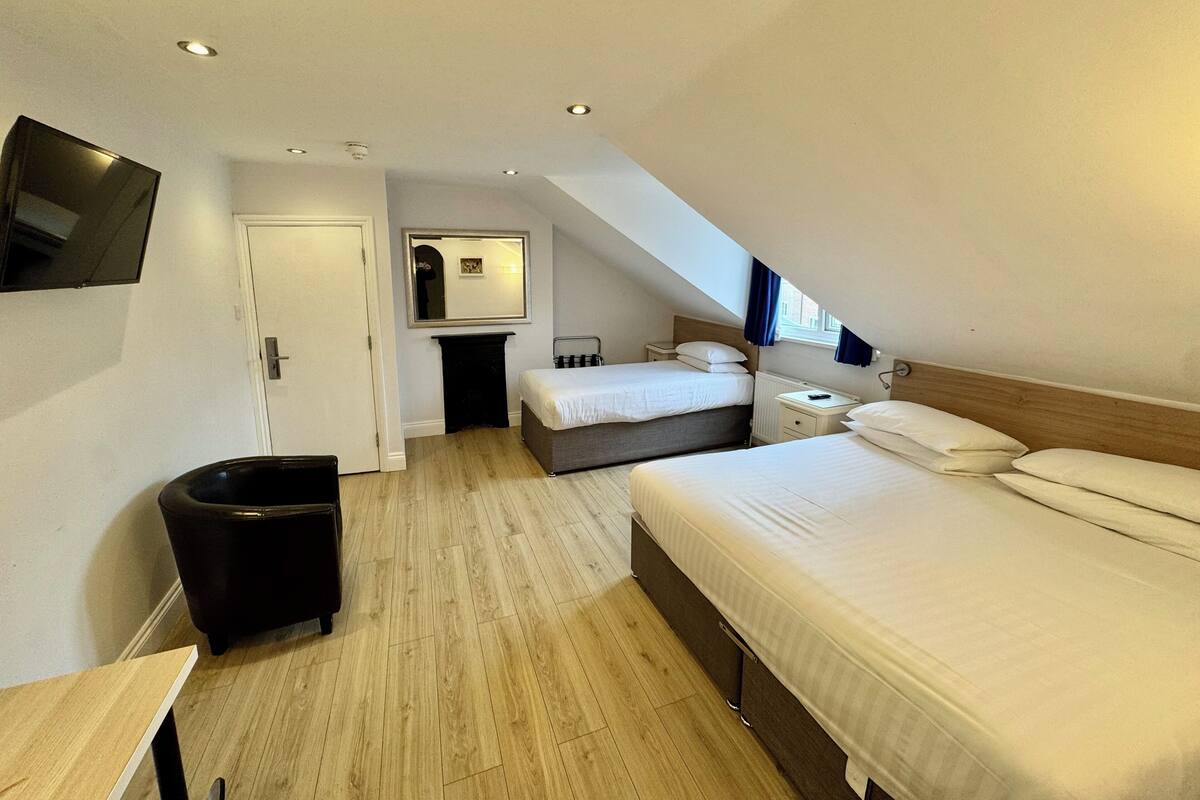 Une chambre d’hôtel moderne avec un plafond de style industriel, un grand lit, une petite table de chevet, une chaise et un téléviseur fixé au mur.