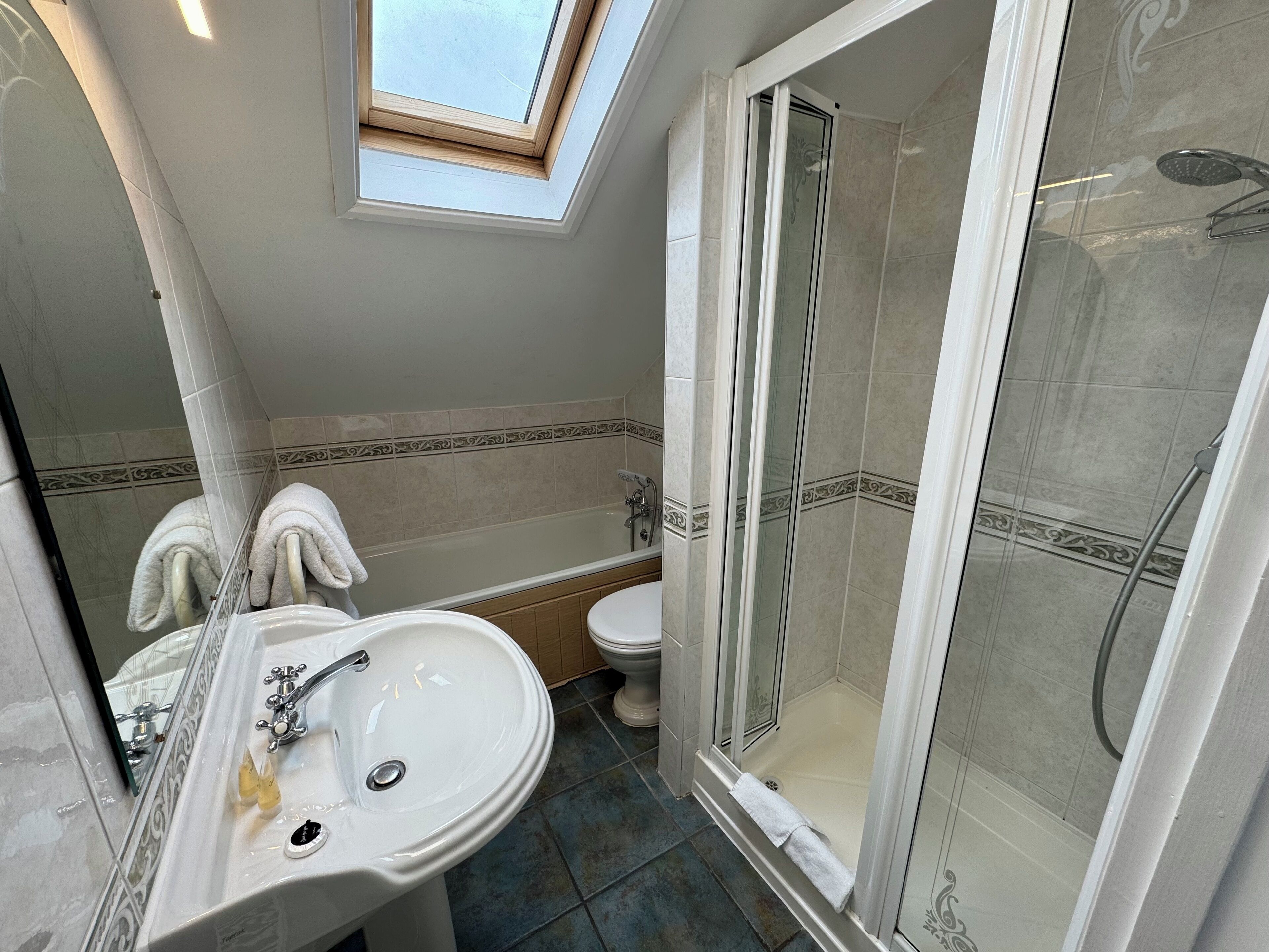 A bathroom with a skylight, a sink, a toilet, and a glass-enclosed shower.