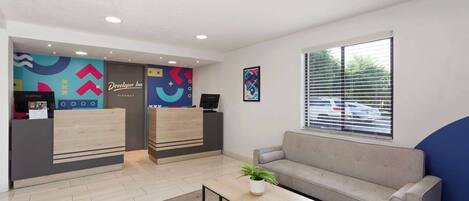 A hotel reception area with a reception desk, a sofa, a coffee table, and a window with blinds.