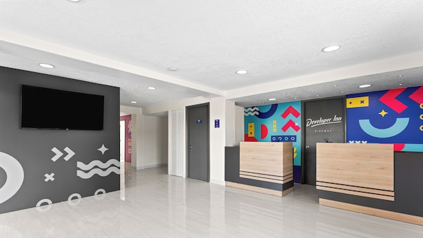 Un hall d’hôtel moderne doté d’un téléviseur à écran plat, d’un comptoir de réception et d’œuvres d’art murales aux motifs géométriques et aux couleurs vives.
