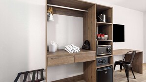Une chambre moderne avec un bureau en bois, une chaise noire, un téléviseur encastré et un petit réfrigérateur.