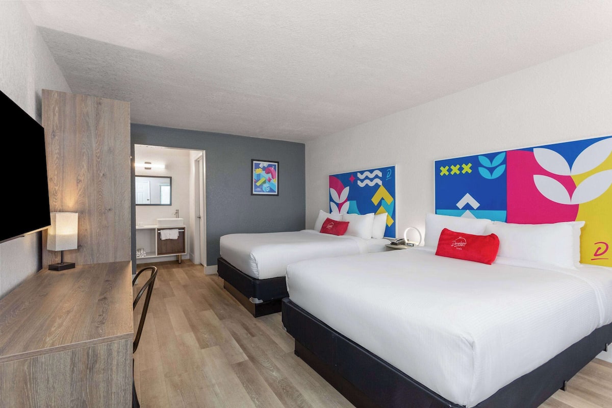A hotel room with two beds, a desk, a TV, and a bathroom.