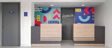 A hotel reception area with a modern design, featuring a colorful abstract wall art and a sign for the Developer Inn.