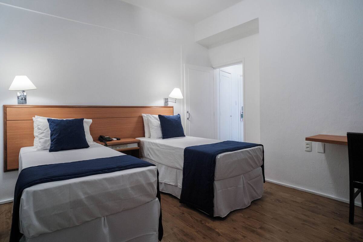 A hotel room with two single beds, wooden headboards, white walls, and a wooden floor.
