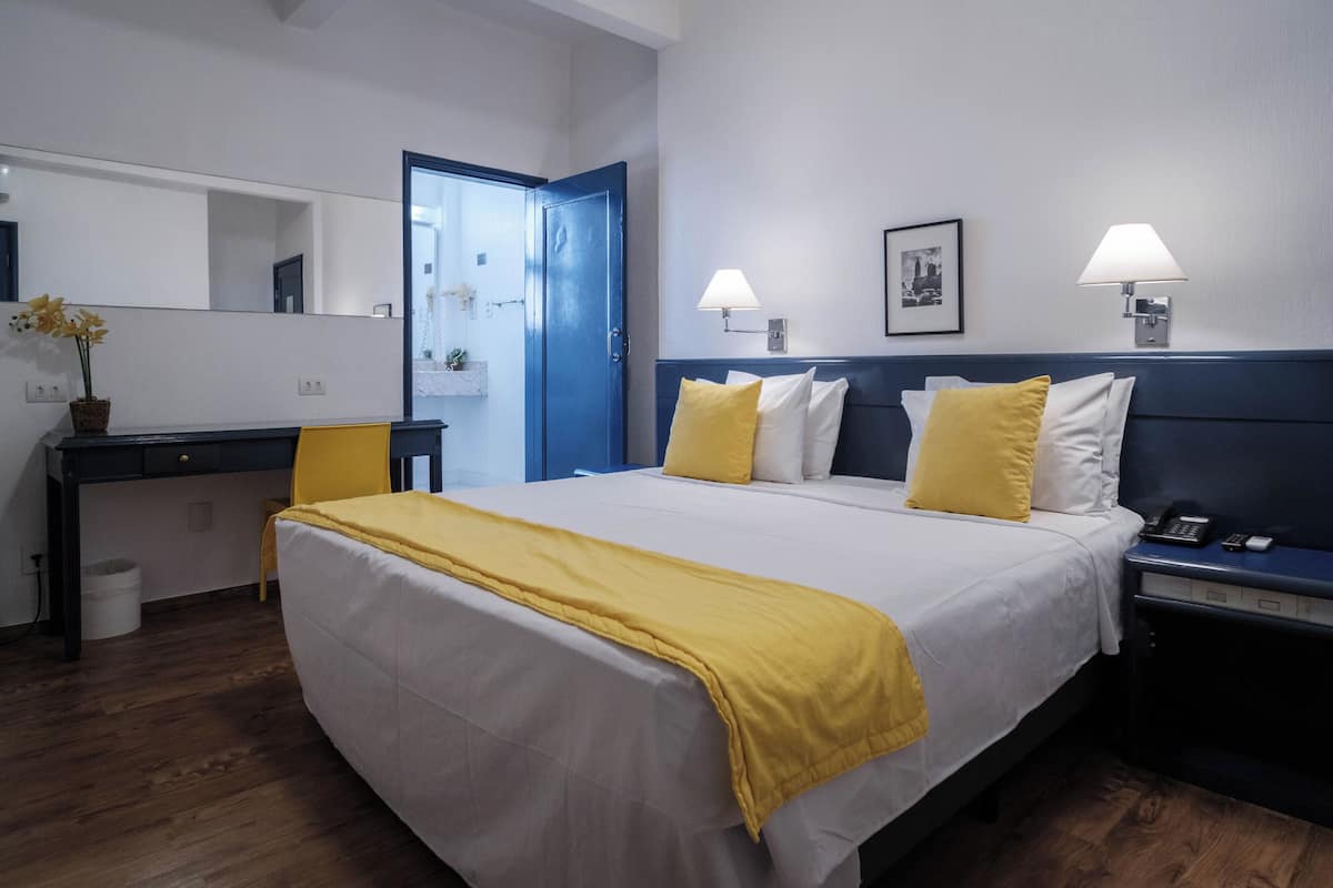A hotel room with a bed, bedside tables, a desk, a chair, a mirror, and a door.