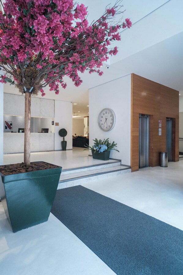 A reception area with a large potted plant, a clock, and a reception desk. - Hotel Normandie by Easy Plus (São Paulo)