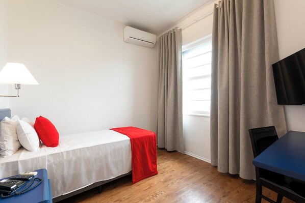 Habitación de hotel con cama, escritorio, silla, lámpara, aire acondicionado y televisión.