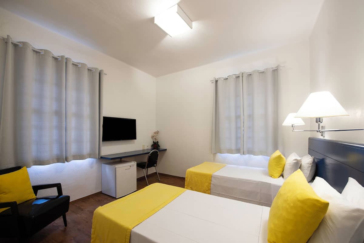 A hotel room with two beds, a desk, a TV, and a lamp.