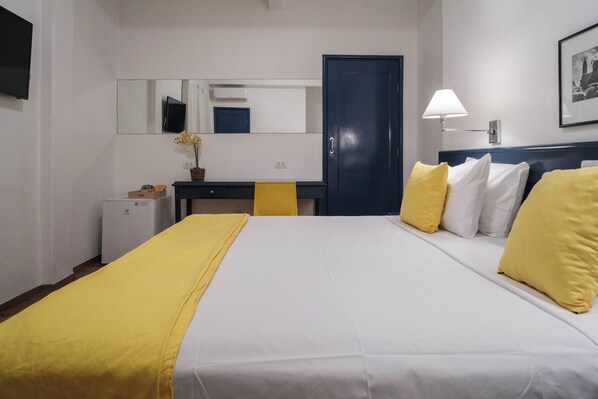 A hotel room with a bed, a desk, a chair, a small refrigerator, a lamp, and a door. - Hotel Normandie by Easy Plus (São Paulo)