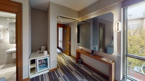 Quarto de hotel com banheiro, minibar, espelho e vista para o exterior.