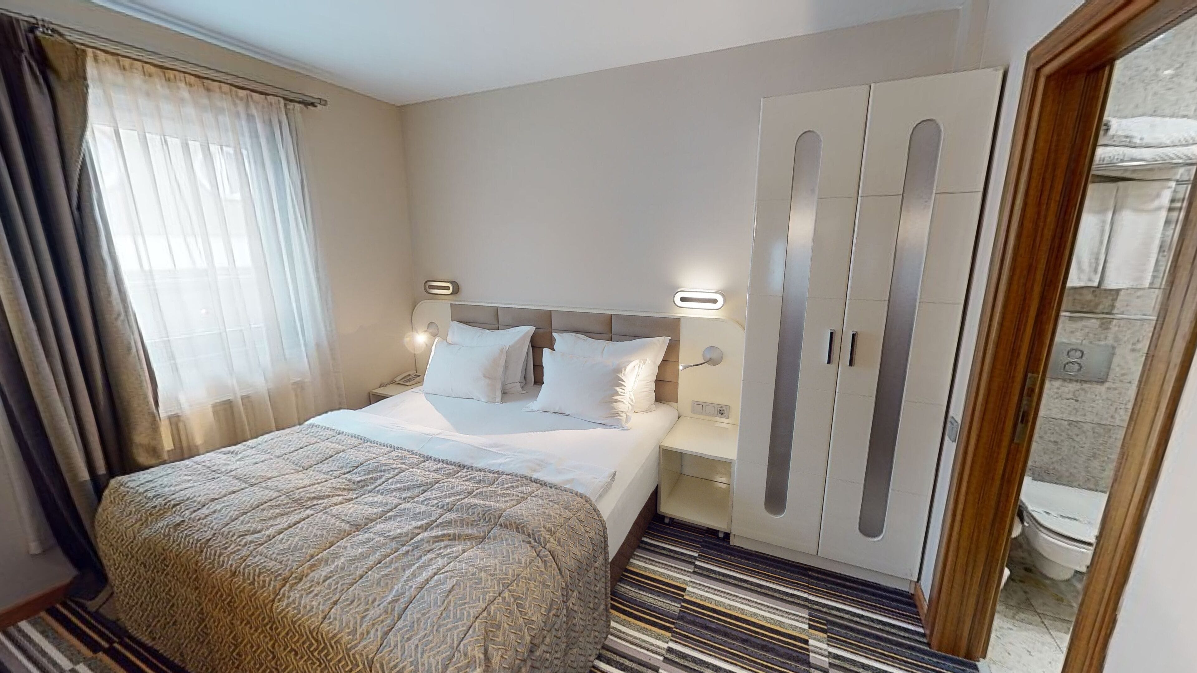 A hotel room with a bed, bedside tables, a wardrobe, and a bathroom visible through an open door.