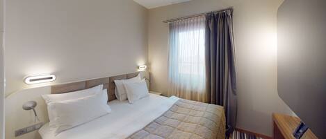 A hotel room with a bed, a bedside table, a nightstand, and a window with curtains.