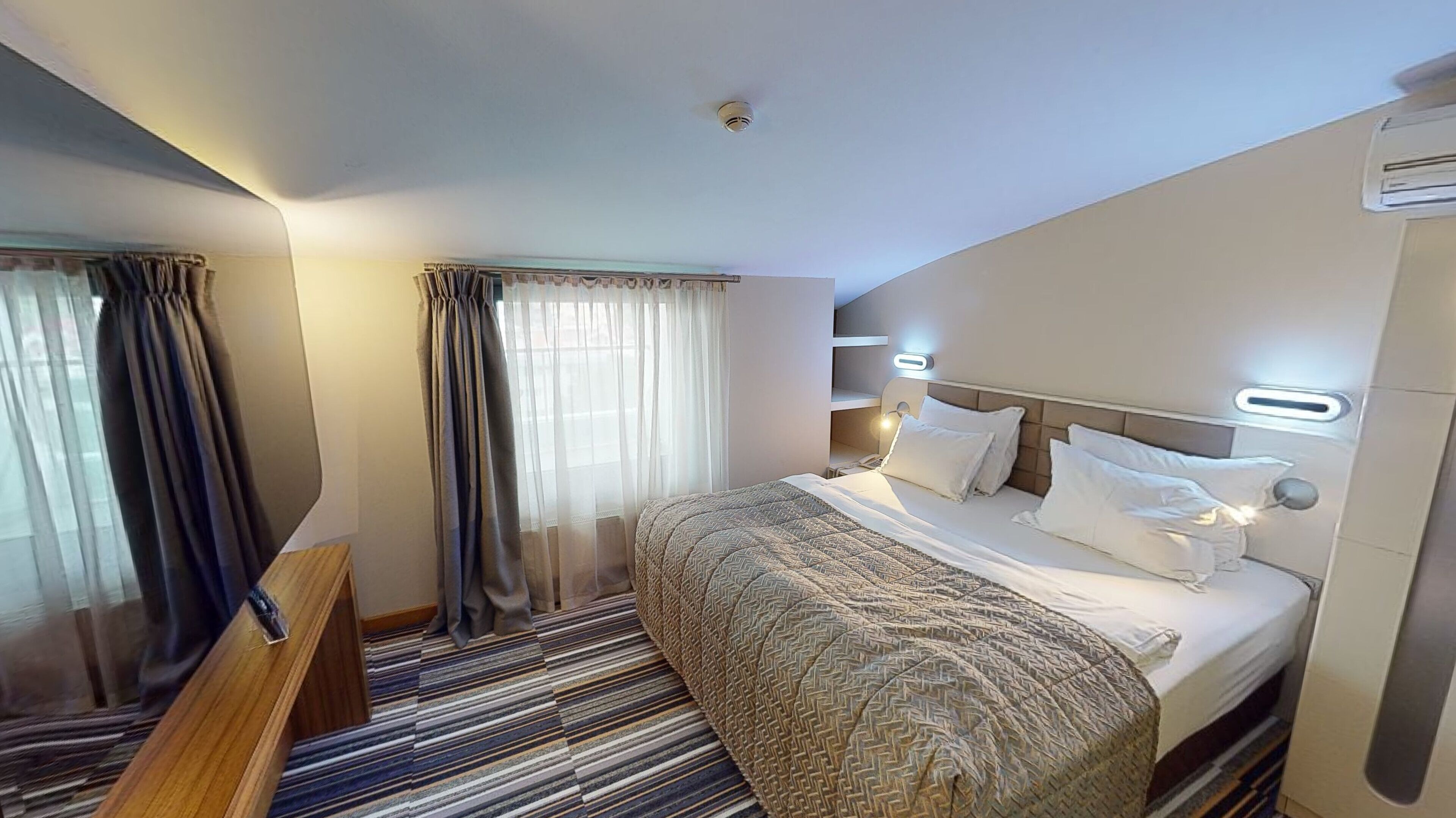 Ein Hotelzimmer mit Bett, Vorhängen, Nachttisch und einem Streifenmuster-Teppich.