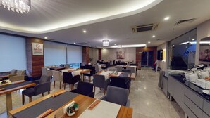 Uma sala de jantar de hotel moderna, com várias mesas e cadeiras, uma tela grande e um candelabro.