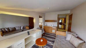 Quarto de hotel moderno com sofá, uma mesa redonda pequena, cozinha compacta e espelho.