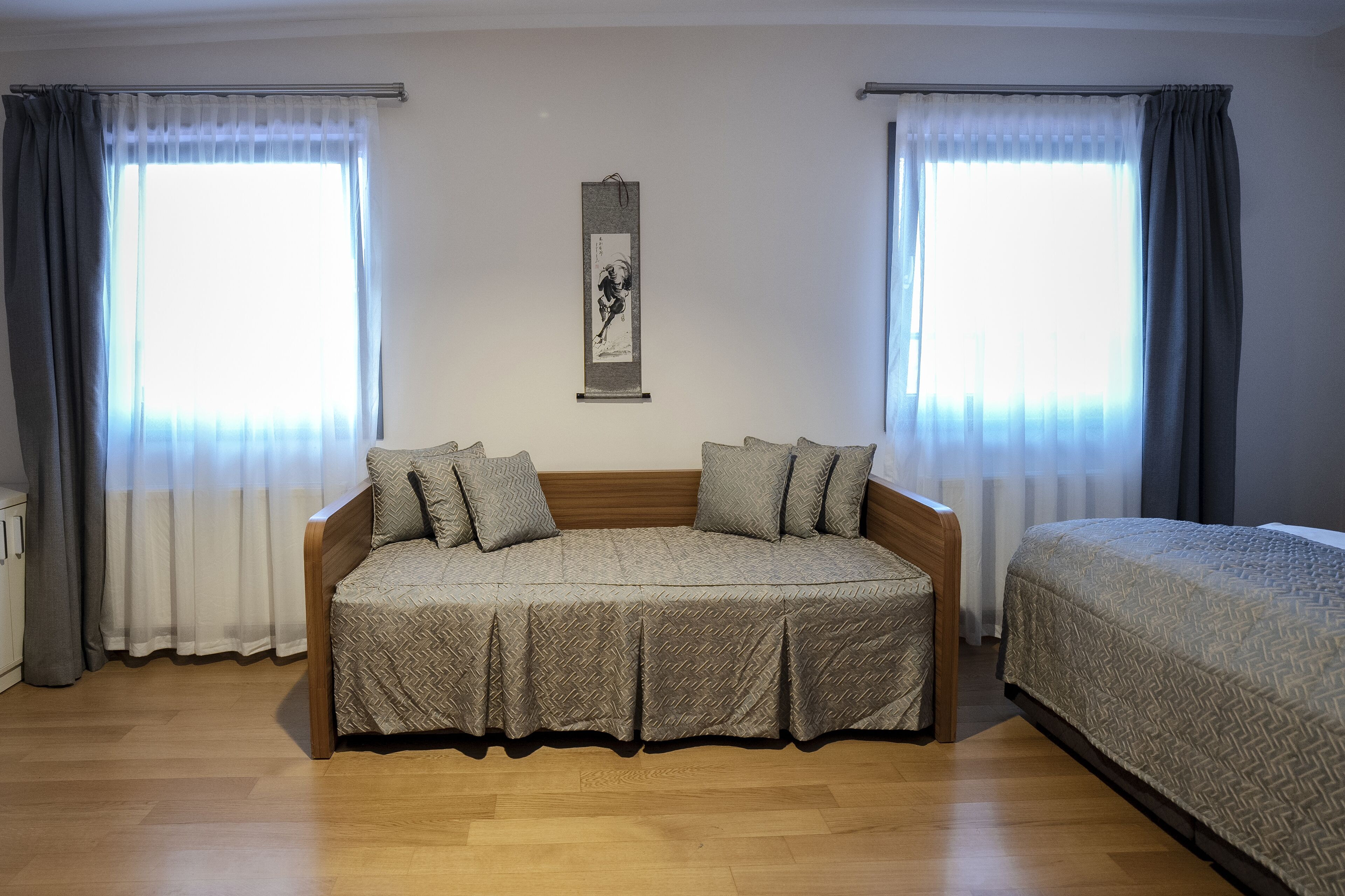A bedroom with a wooden bed, a sofa bed, and two windows with curtains.