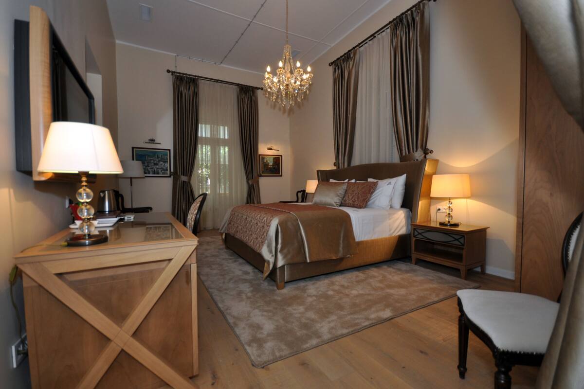 Een hotelkamer met een bed, een bureau, een stoel, een nachtkastje en een kroonluchter.