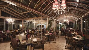 Um restaurante amplo com pé-direito alto, lustres e várias mesas de jantar dispostas para os hóspedes.