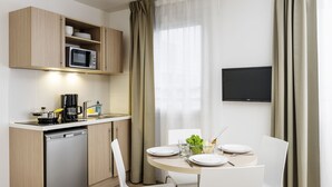 A compact kitchen with a microwave, coffee maker, and dishwasher. There is a dining table with chairs and a TV mounted on the wall. - Aparthotel Adagio Access Paris Clichy (Clichy)