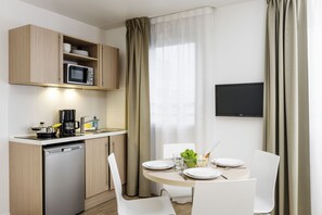 A compact kitchen with a microwave, coffee maker, and dishwasher. There is a dining table with chairs and a TV mounted on the wall.