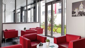 A modern interior with red seating, a white table, and a view of the outdoors through large windows. - Aparthotel Adagio Access Paris Clichy (Clichy)