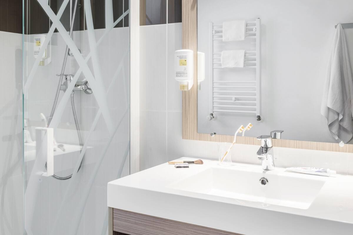 A modern bathroom with a glass shower enclosure, a white sink, and a towel rack.