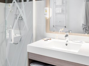 A modern bathroom with a glass shower enclosure, a white sink, and a mirror with a towel rack. - Aparthotel Adagio Access Paris Clichy (Clichy)