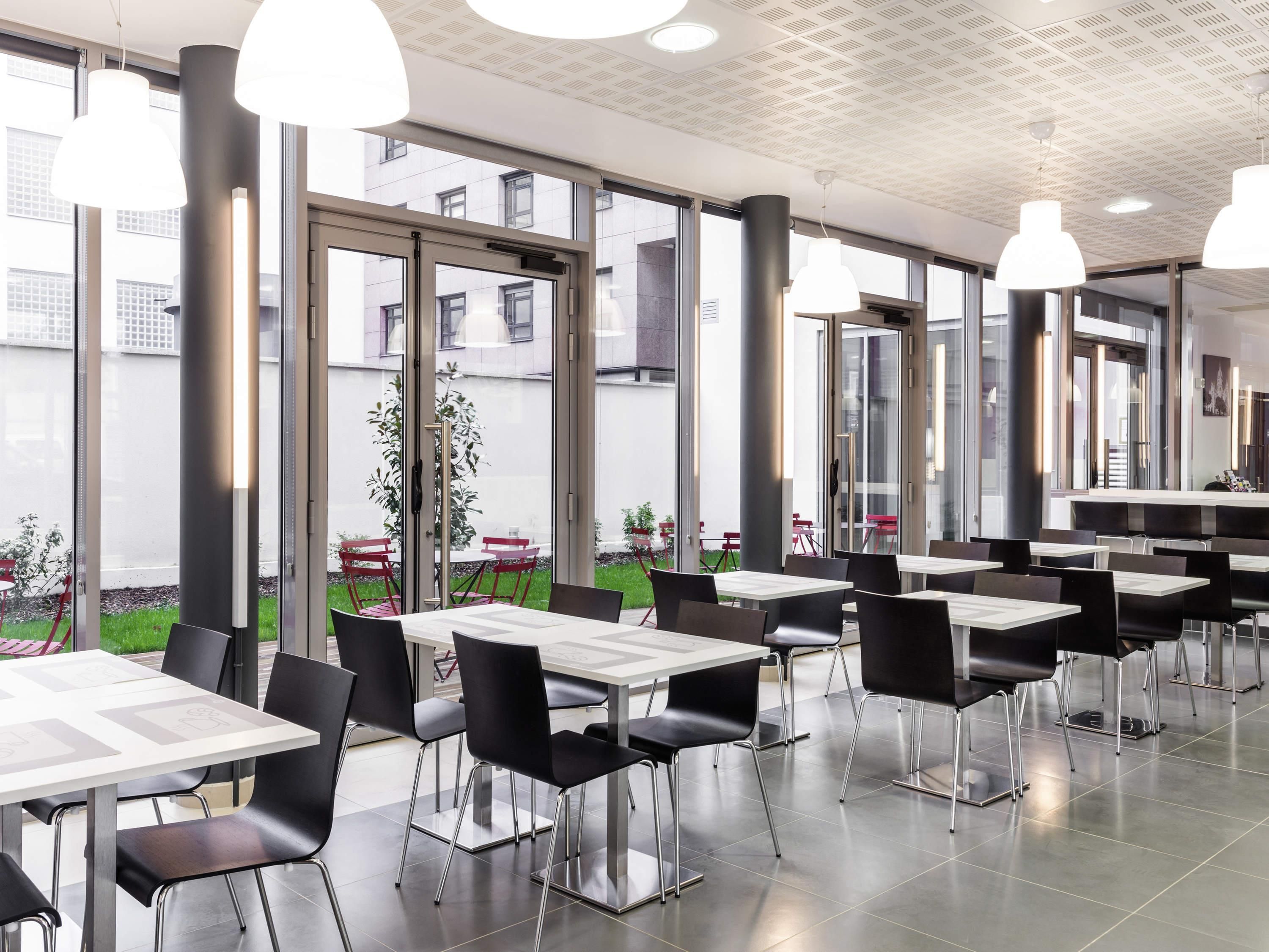 A modern dining area with tables and chairs, large windows, and pendant lighting.