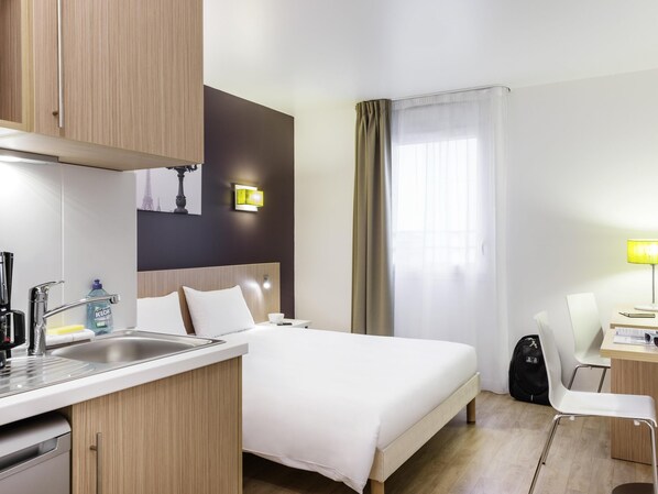 A hotel room with a bed, a desk, a chair, a sink, and a window with curtains.