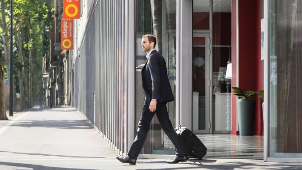 A man in a suit walking past a building with a modern design, a glass entrance, and a sign for 'adagio aparthotel'. - Aparthotel Adagio Access Paris Clichy (Clichy)