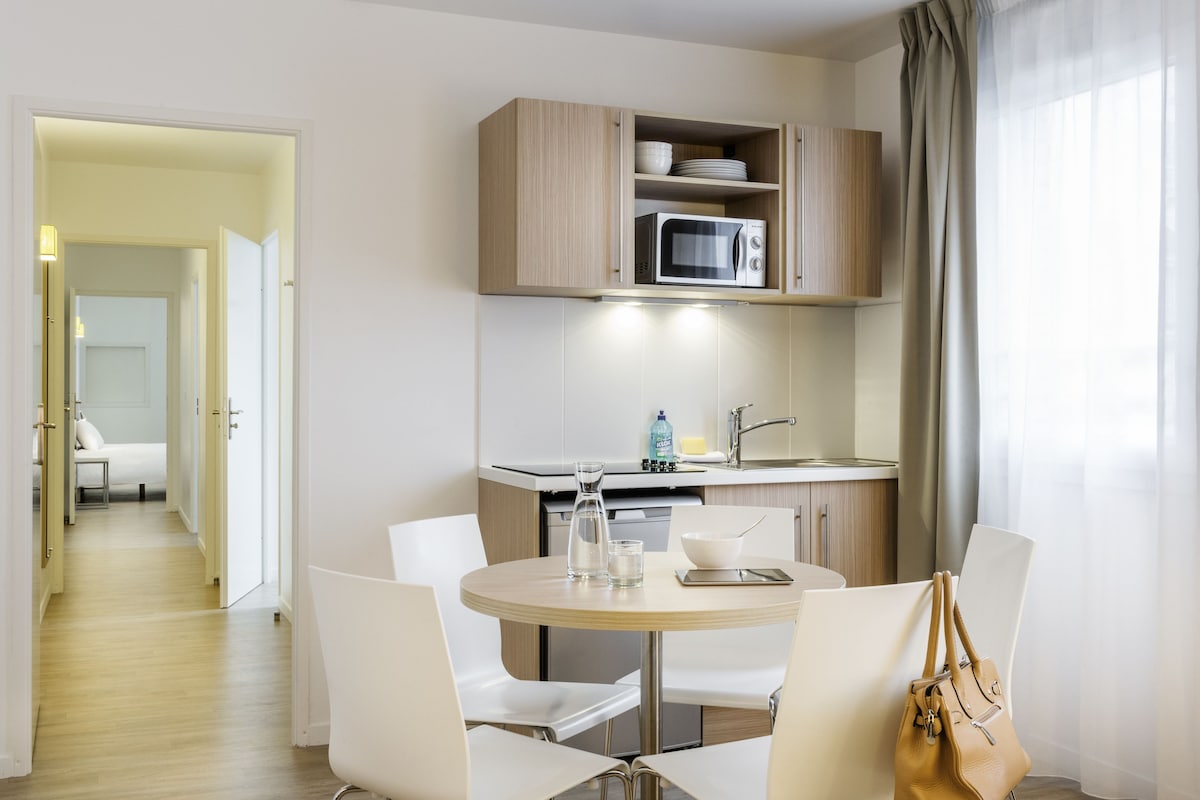 Une chambre d’hôtel moderne dotée d’un coin repas, d’une kitchenette et d’une salle de bain.