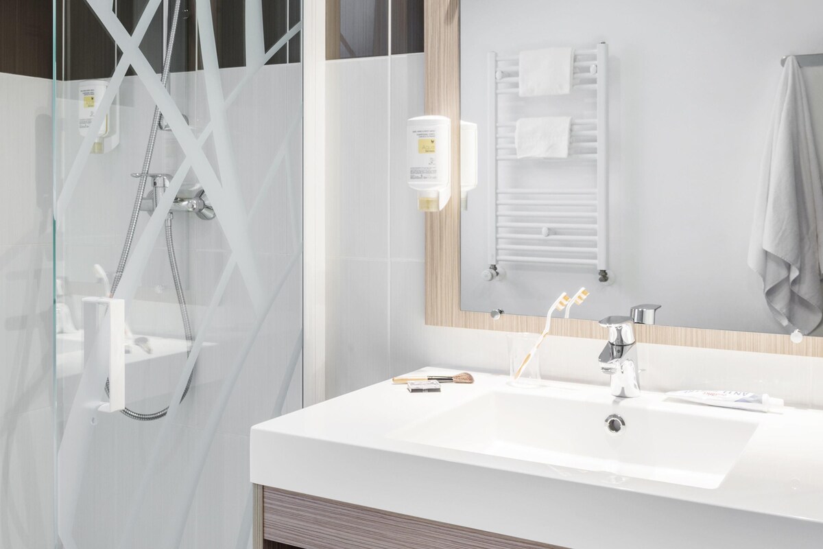 Un bagno moderno con cabina doccia in vetro, un lavandino bianco e un porta asciugamani.