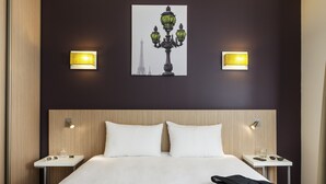 A hotel room with a bed, two bedside tables, a nightstand, a wall-mounted lamp, and a framed picture of the Eiffel Tower. - Aparthotel Adagio Access Paris Clichy (Clichy)