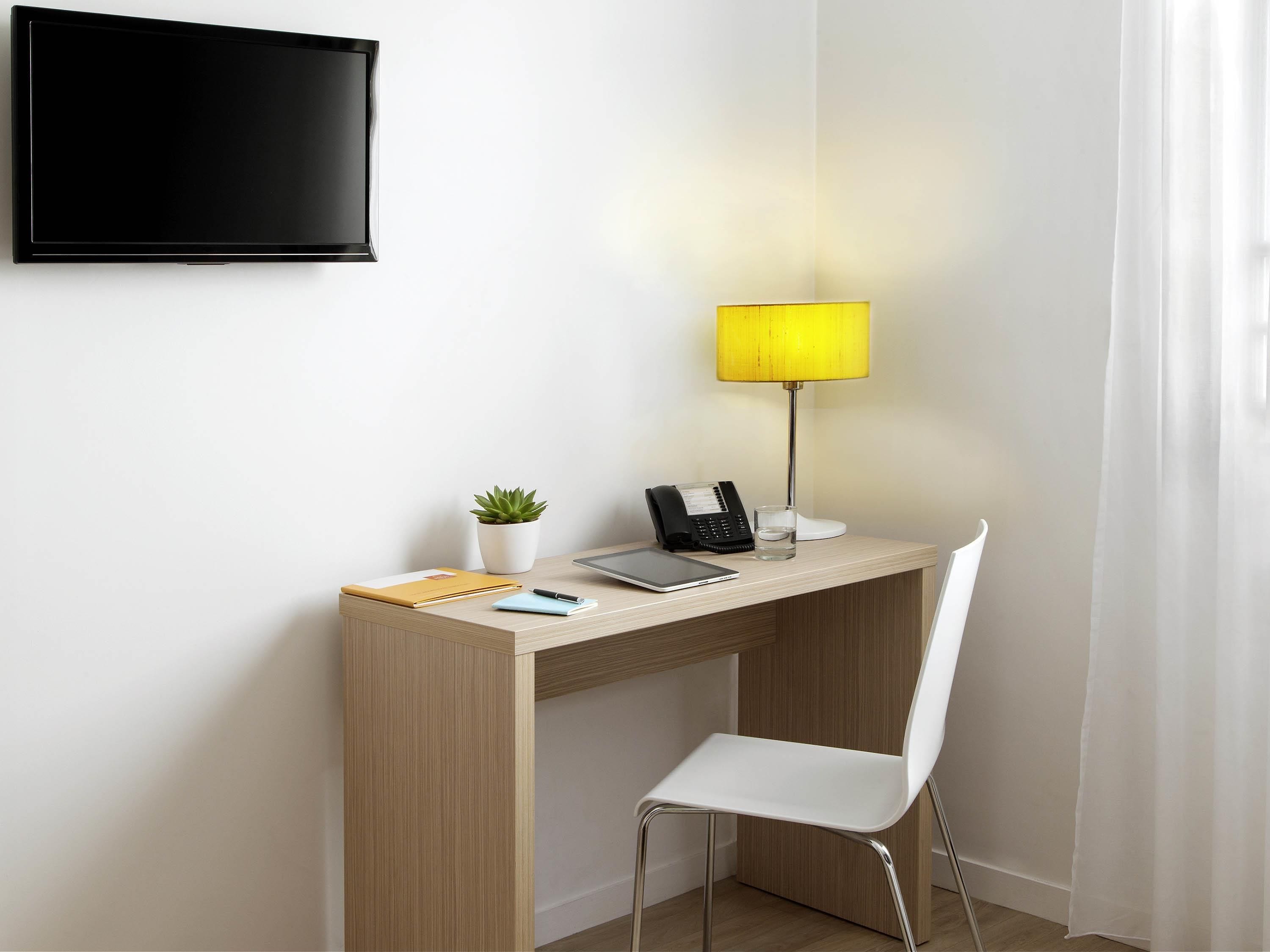 Un bureau moderne avec une lampe, un téléphone, un verre d’eau, un carnet et une plante.