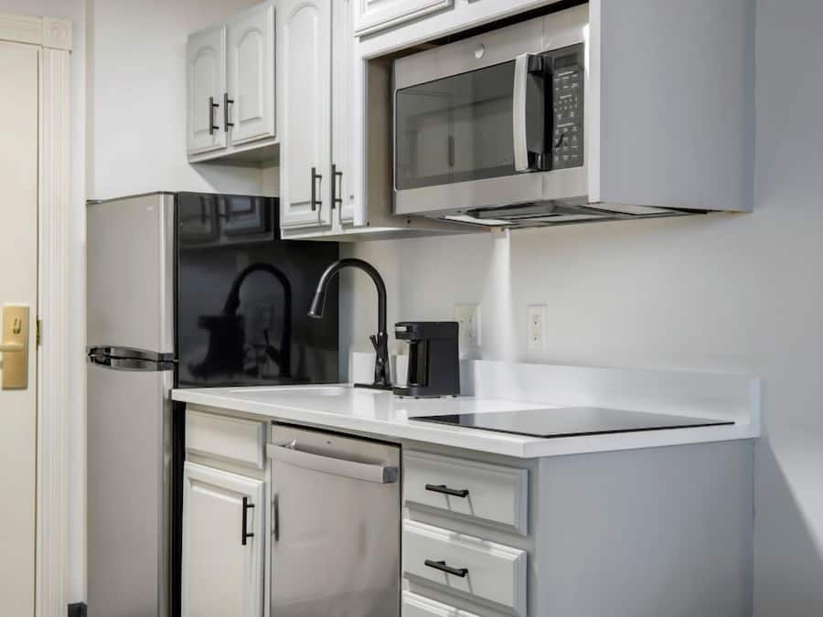 A compact kitchen with white cabinetry, a stainless steel refrigerator, a microwave, and a sink.