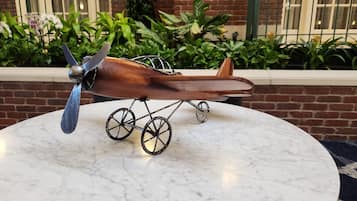 Un avión modelo sobre una mesa de mármol, con un muro de ladrillo y follaje al fondo.