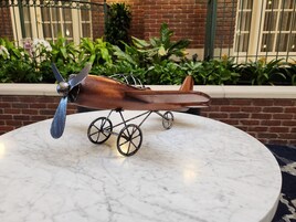 Un avión modelo sobre una mesa de mármol, con un muro de ladrillo y follaje al fondo.