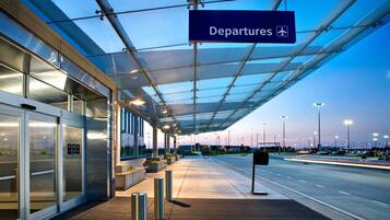 An airport departure area with a covered walkway, glass doors, and a clear sky.