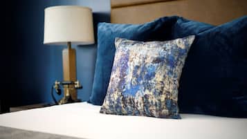 Una cama con sábana blanca, almohada azul y lámpara con pantalla color beige.
