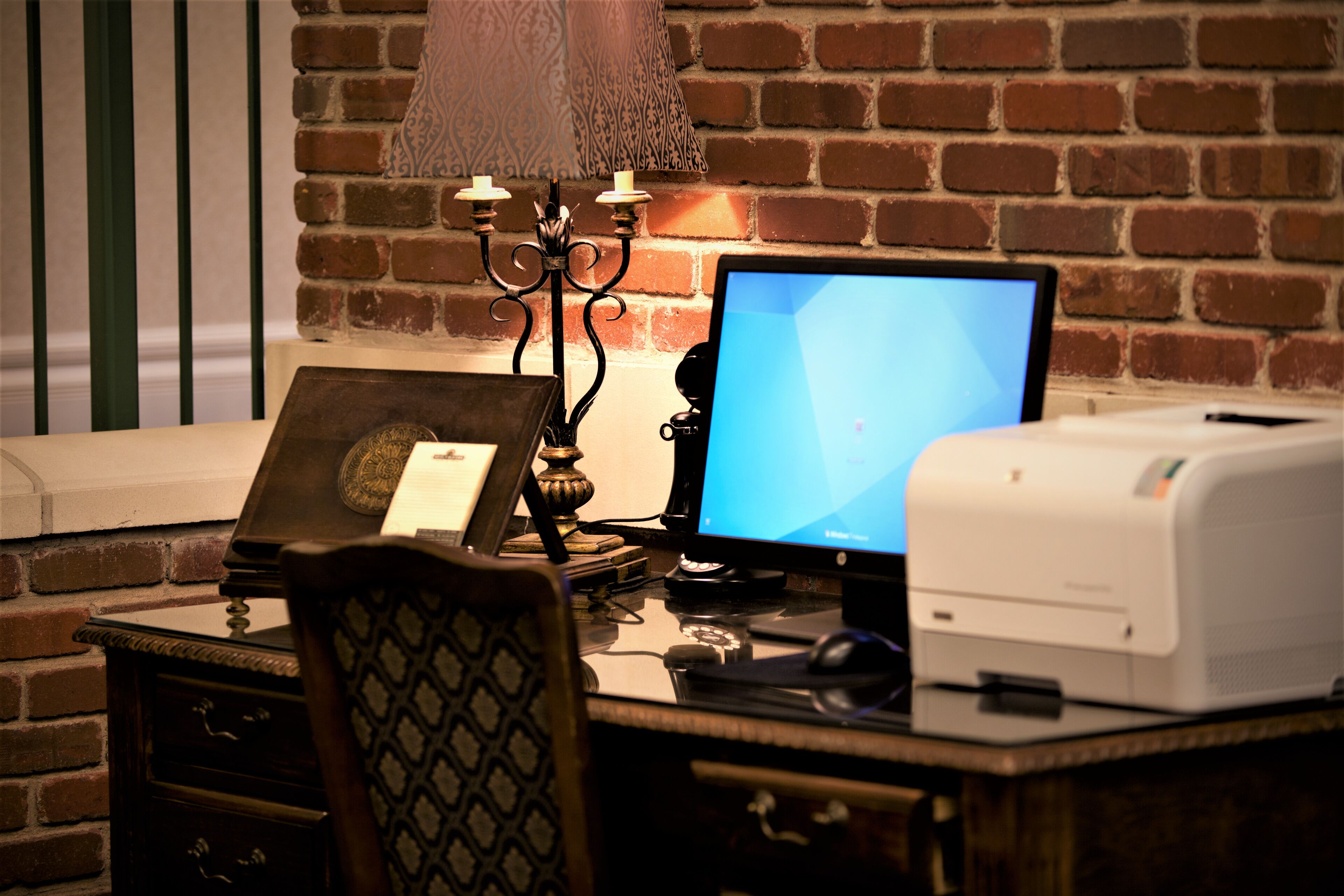 A desk with a computer, printer, and decorative items against a brick wall.