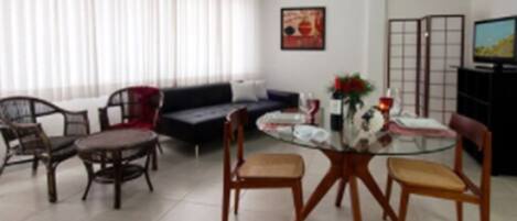 A living room with a sofa, dining table, chairs, and a TV.