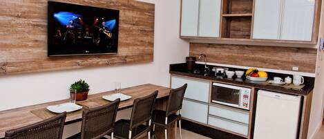 Cocina pequeña con una mesa de comedor de madera, sillas de mimbre, televisor integrado y un refrigerador compacto.