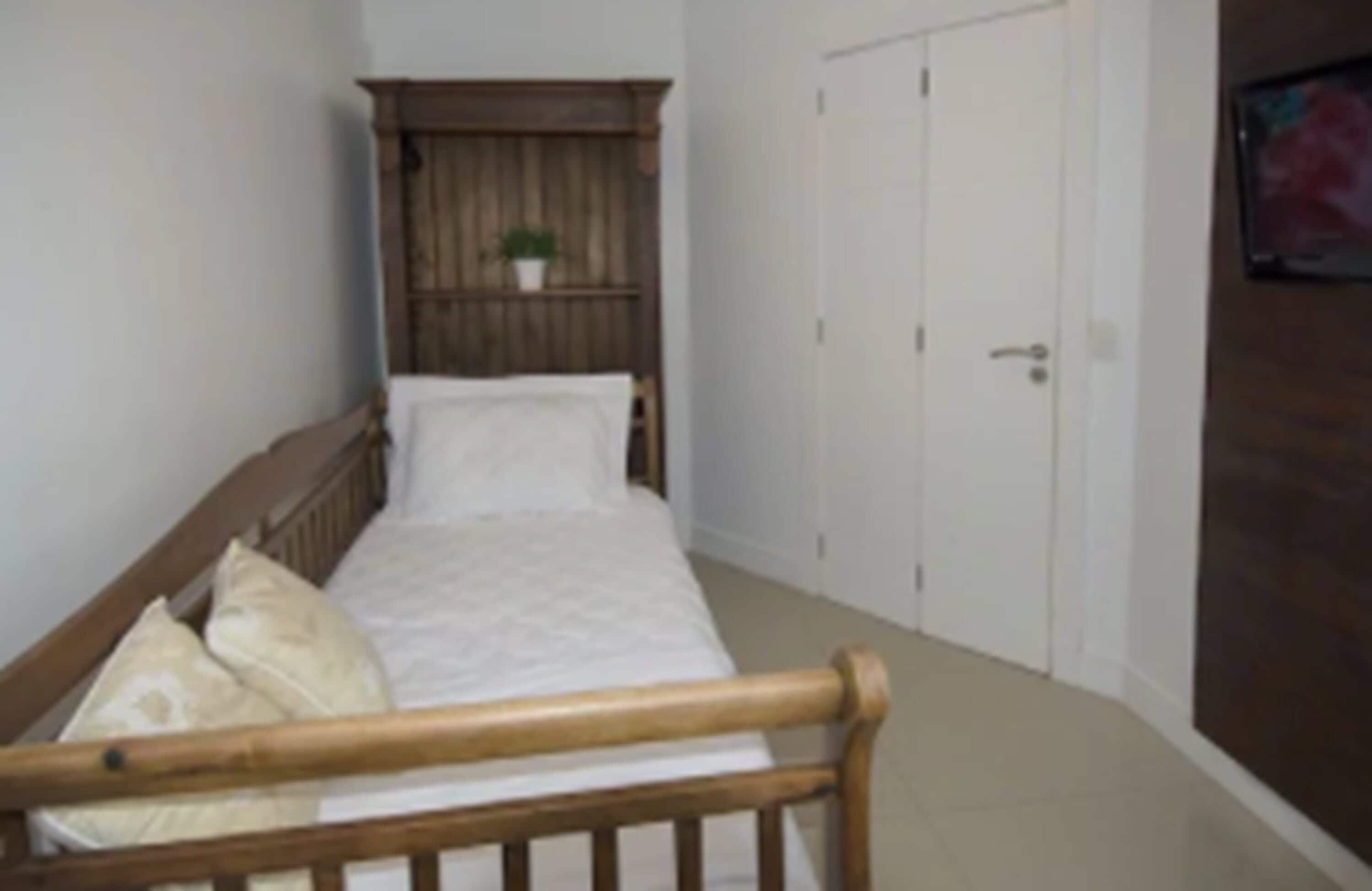 Quarto pequeno com cama de madeira, um guarda-roupa e uma pequena planta em vaso.