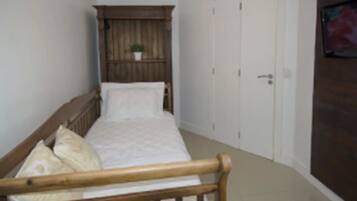 Quarto pequeno com cama de madeira, um guarda-roupa e uma pequena planta em vaso.