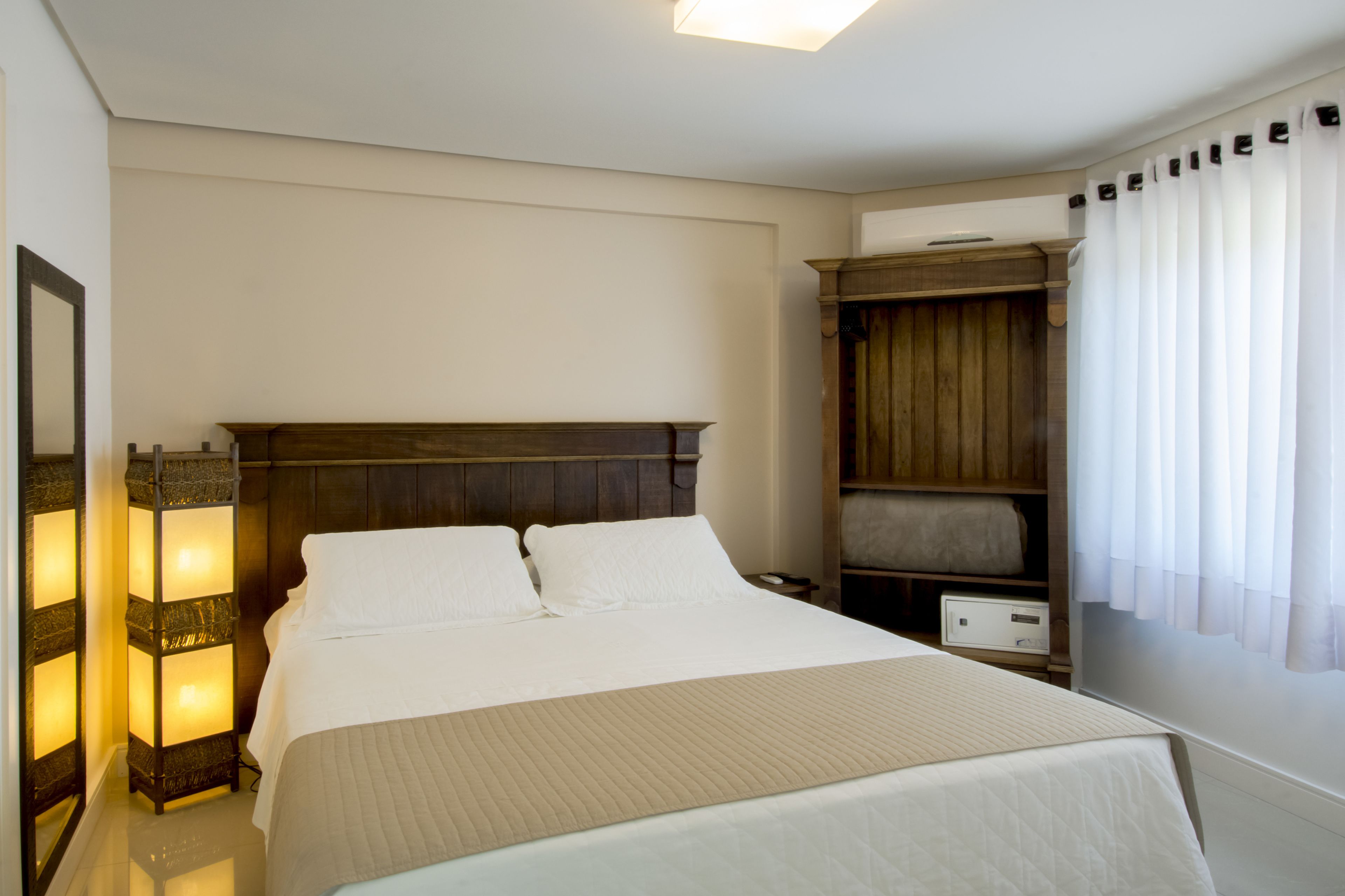 A neatly arranged hotel room with a large bed, bedside tables, a wardrobe, and a nightstand.