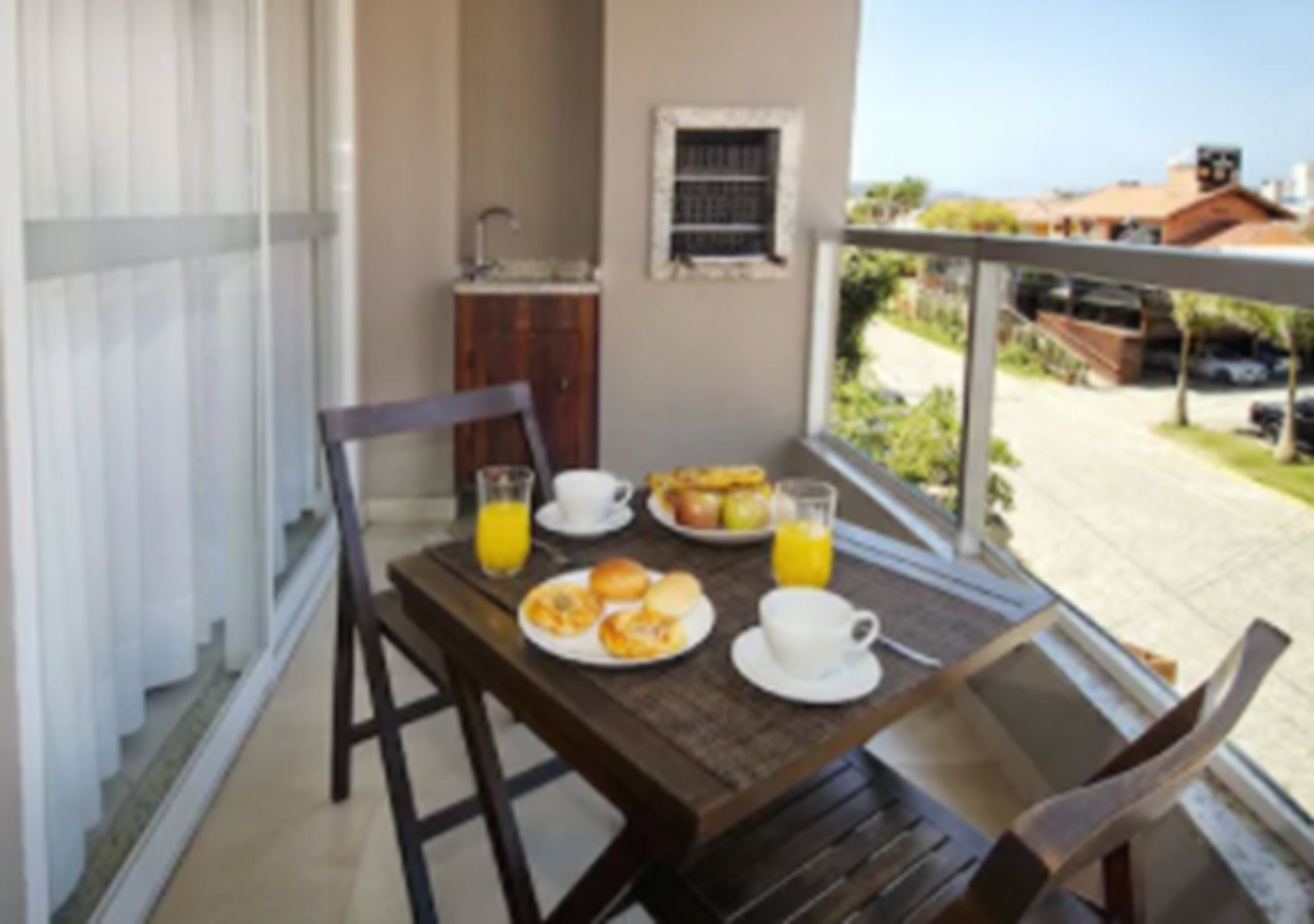 A balcony with a table set for breakfast, including plates of food and drinks, and a view of the surrounding area.