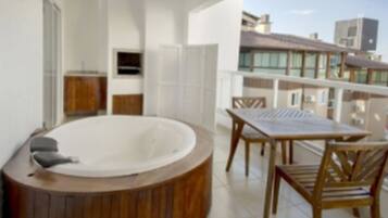 Un balcón con un jacuzzi de madera, una mesa y sillas.